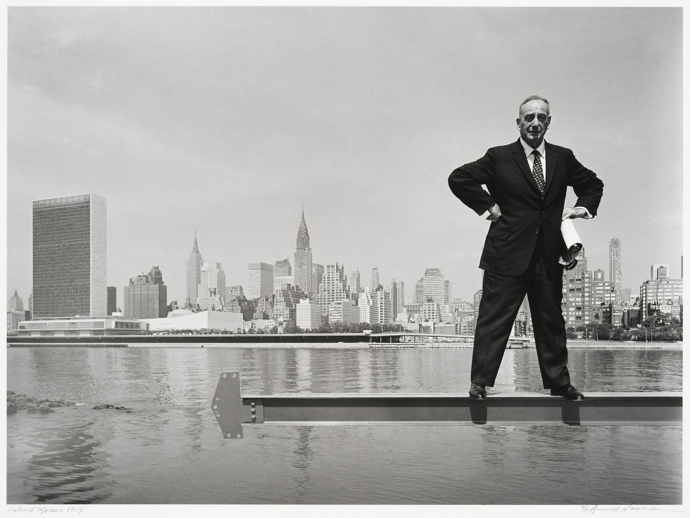 Portrait of Robert Moses standing on steel frame, above the East River with a panoramic view of midtown Manhattan - the United Nations building up to U rollstton Place, New York City, New York