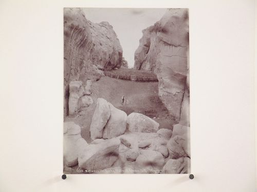 View through a canyon showing fences and a man riding a donkey down an embankment, Acoma, New Mexico, United States