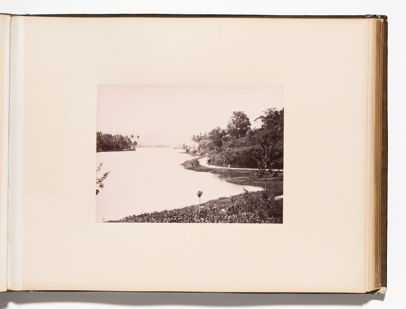 View of a lake, probably Kandy Lake, with a road on the right, Kandy, Ceylon (now Sri Lanka)