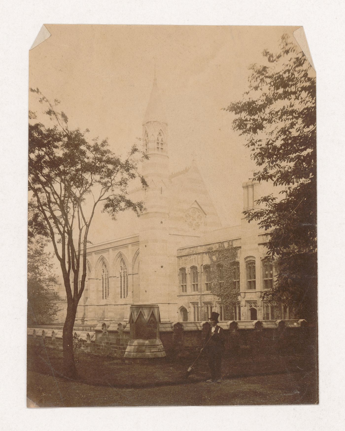 Partial view of a church taken from outside the churchyard wall with a man wearing a top hat in the foreground, England [?]