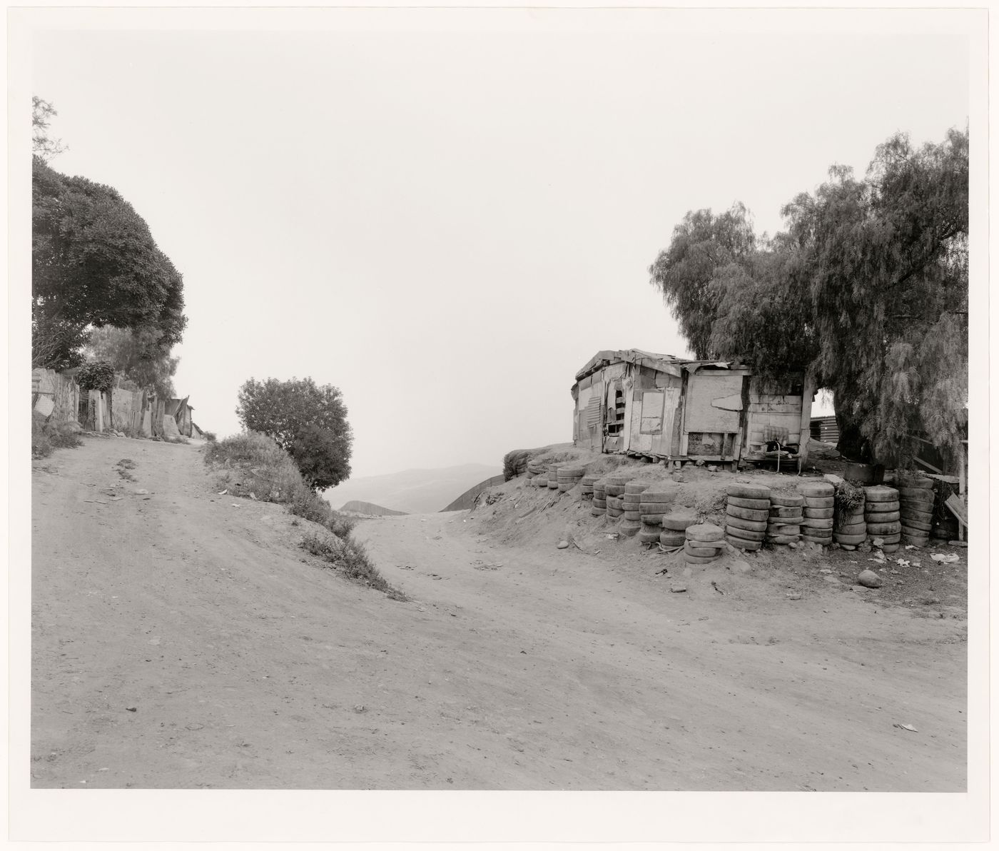 View of dirt road and dwelling showing a partial view of United States-Mexico border fence, San Diego County, California, United States and Colonia Libertad, Tijuana, Baja California, Mexico