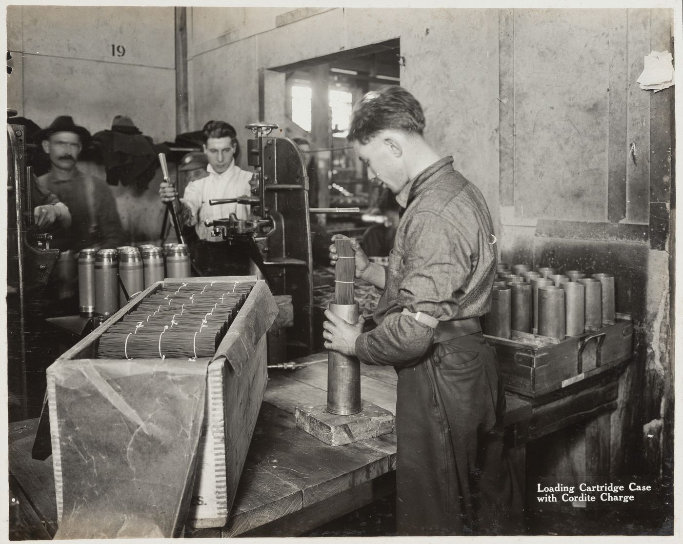 Interior view of workers loading cartridge case with cordite charge at the Energite Explosives Plant No. 3, the Shell Loading Plant, Renfrew, Ontario, Canada