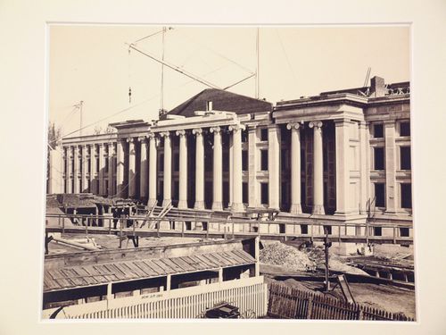 Treasury Building under contruction: Two figures on surrounding walkway, crane on roof, Washington, District of Columbia