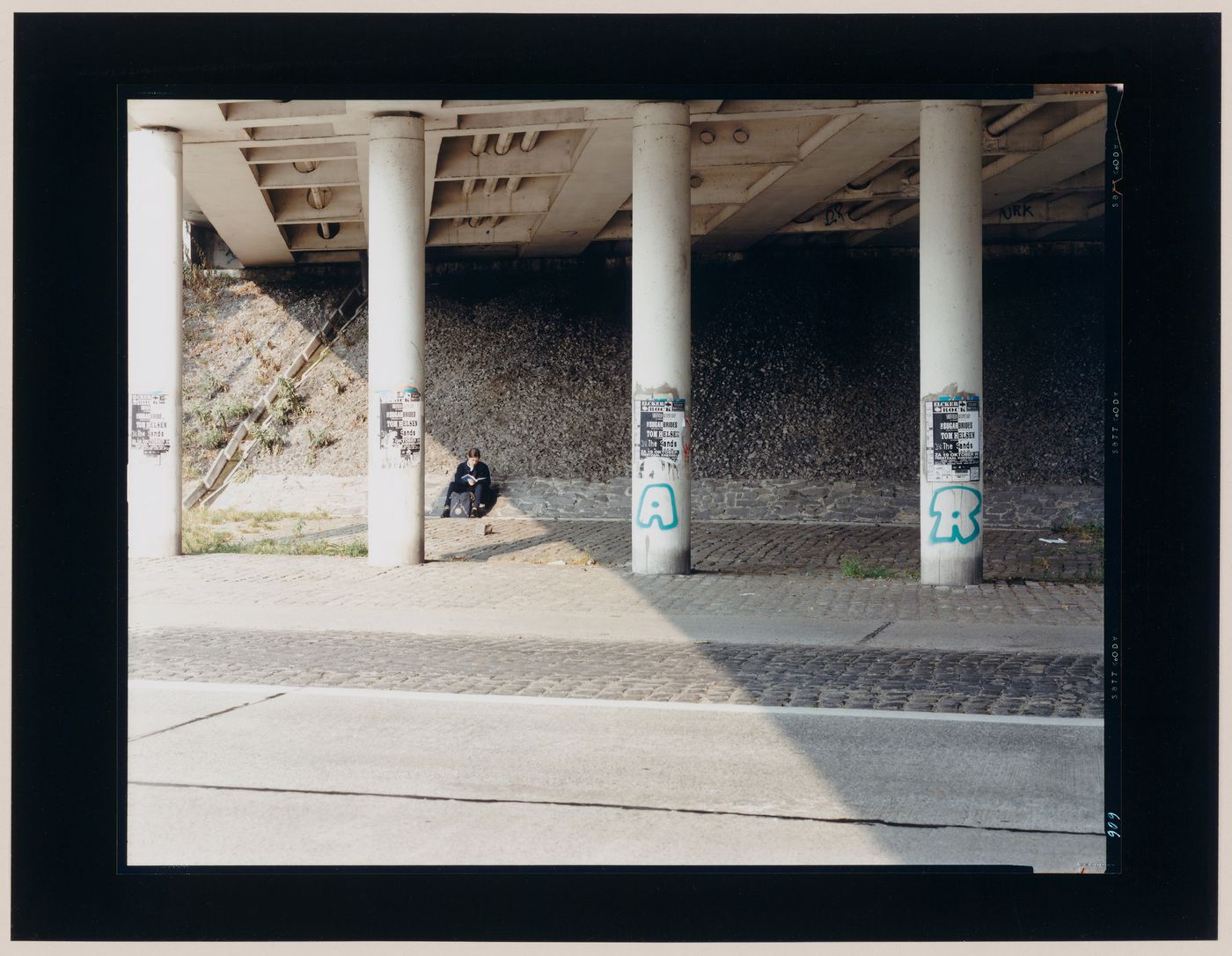 Portrait of a young woman reading showing the roadside under an overpass and columns, Jülich, Germany (from the series "In between cities")