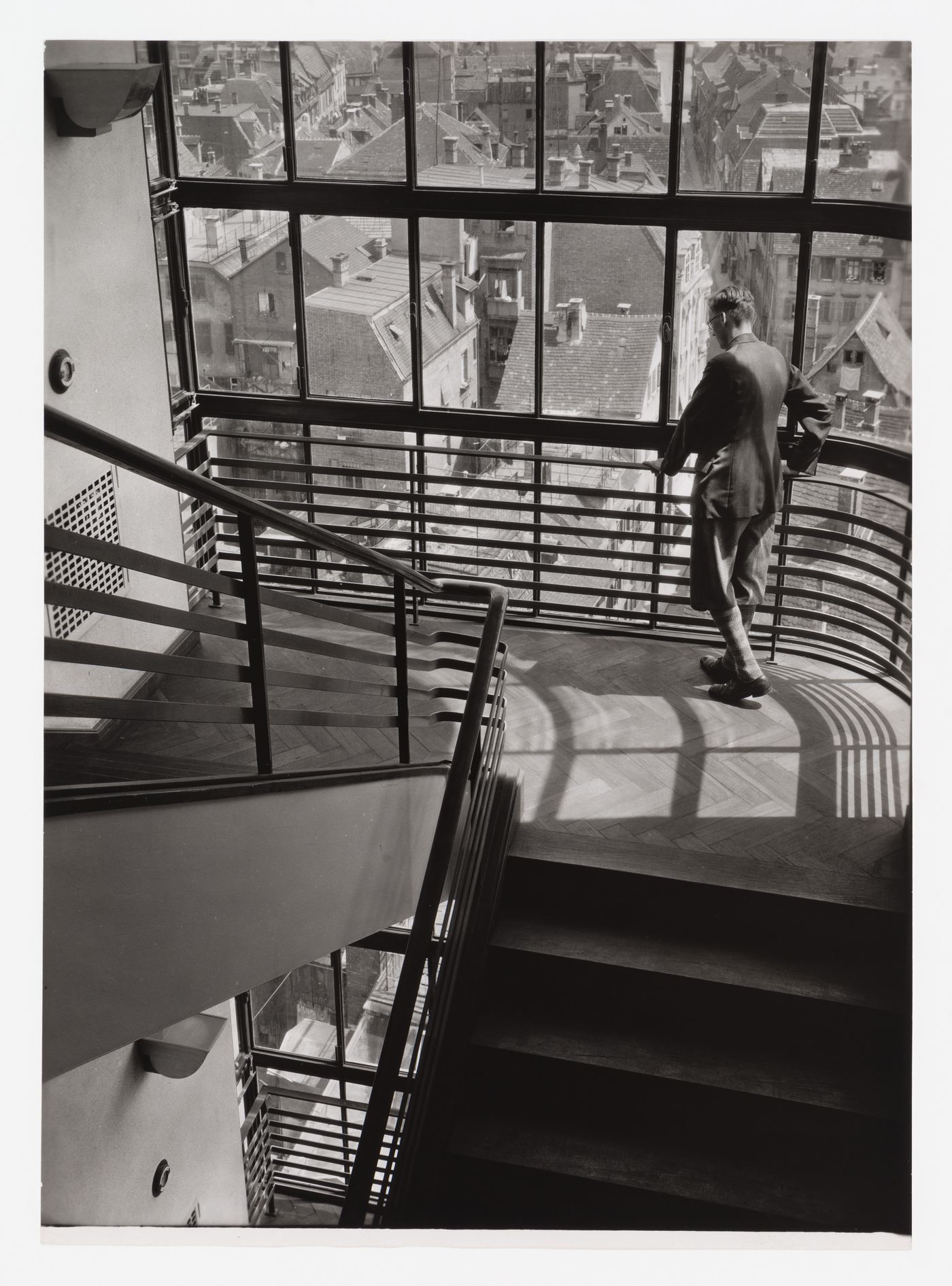 Interior of Kaufhaus Breminger detail of stairwell, with man in knickerbockers at railing, and view of roofs and town, Germany