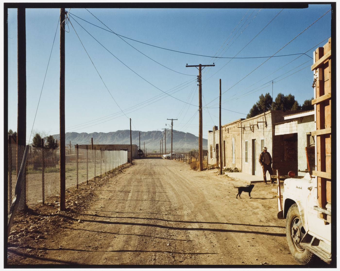 View of a back road with buildings, a man wearing a cowboy hat and a dog, Presidio, Texas