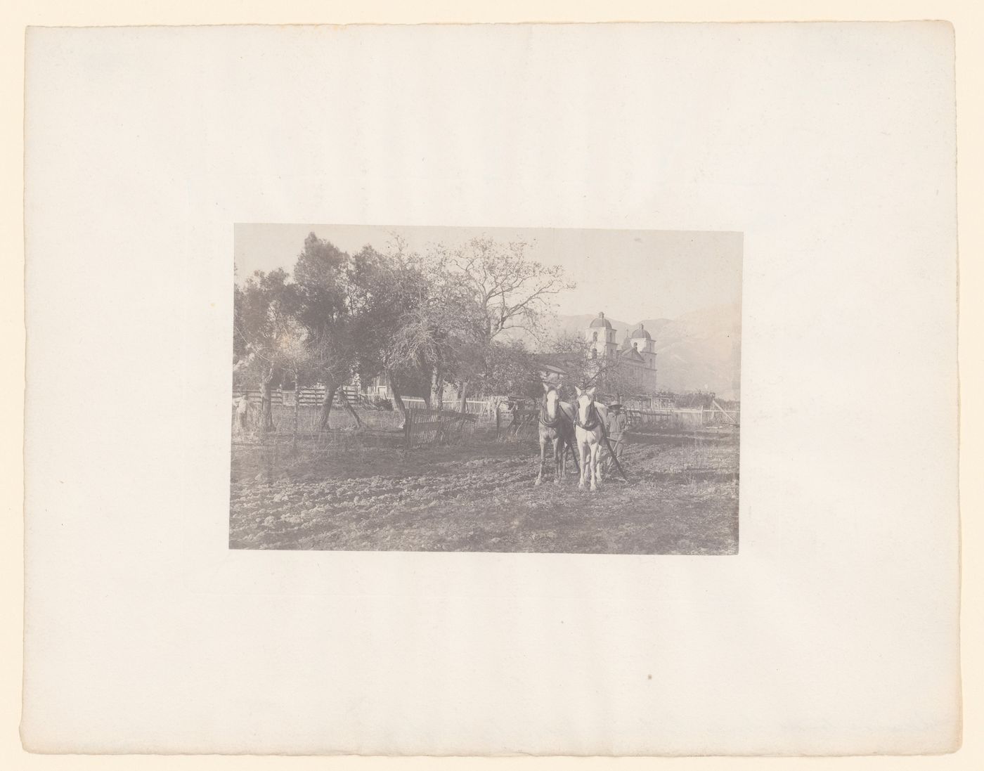 View of the Mission Santa Barbara, with an Indigenous, possibly Chumash, person ploughing mission garden with church in the background, Santa Barbara, California, United States