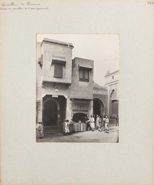 View of people gathered around stand near entrance to pavilion of the Direction de l'enseignement, Tunisian section, Exposition universelle, 1900, Paris France