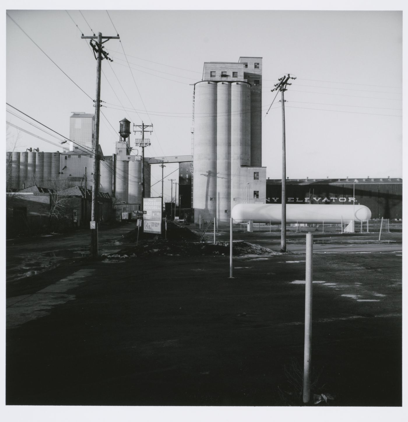 Grain elevator complex with telephone poles and parking lot in foreground, Minneapolis, Minnesota
