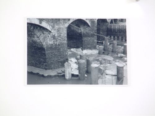 View of reinforced concrete columns in water next to stone arch bridge