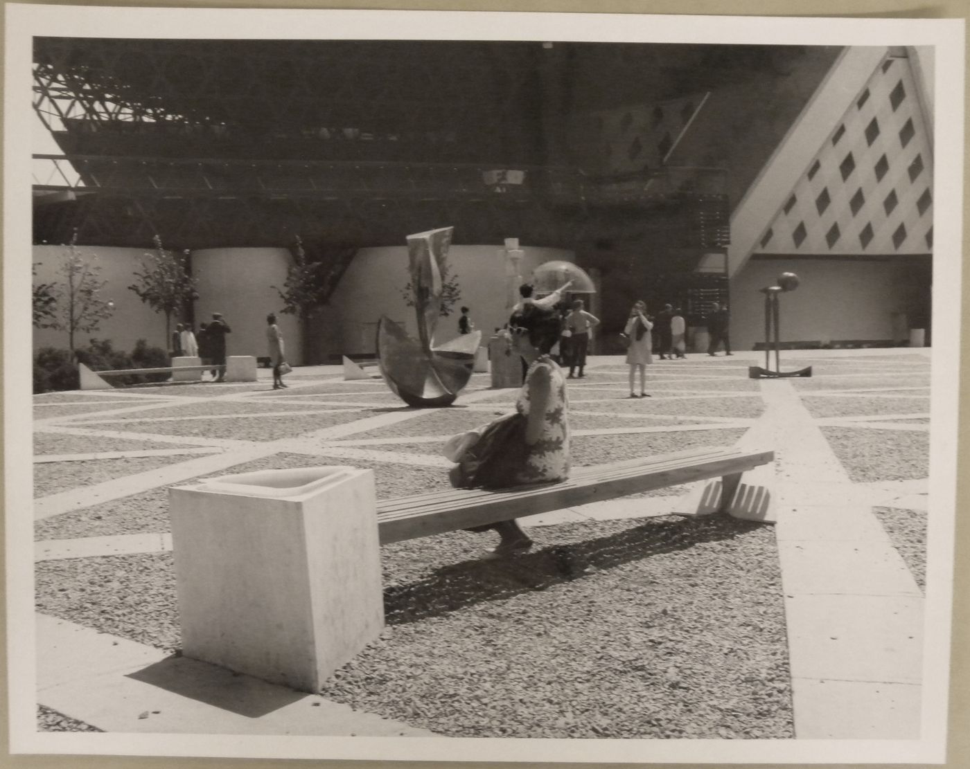 View of a visitor sitting on a bench with sculptures in background, Expo 67, Montréal, Québec