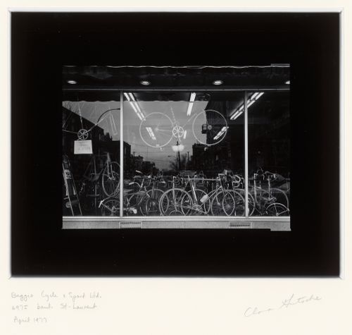 View of a display window of the Baggio Cycle & Sport store showing bicycles and the reflection of avenue Mozart, 6975 boulevard Saint-Laurent, Montréal, Québec