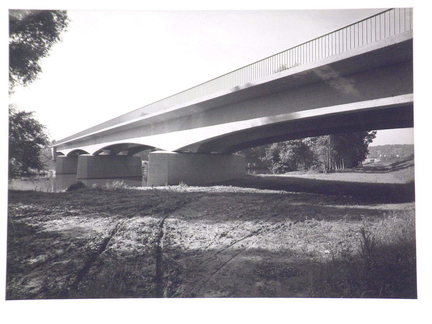 View from river bank of concrete bridge resting on piers, crossing small river