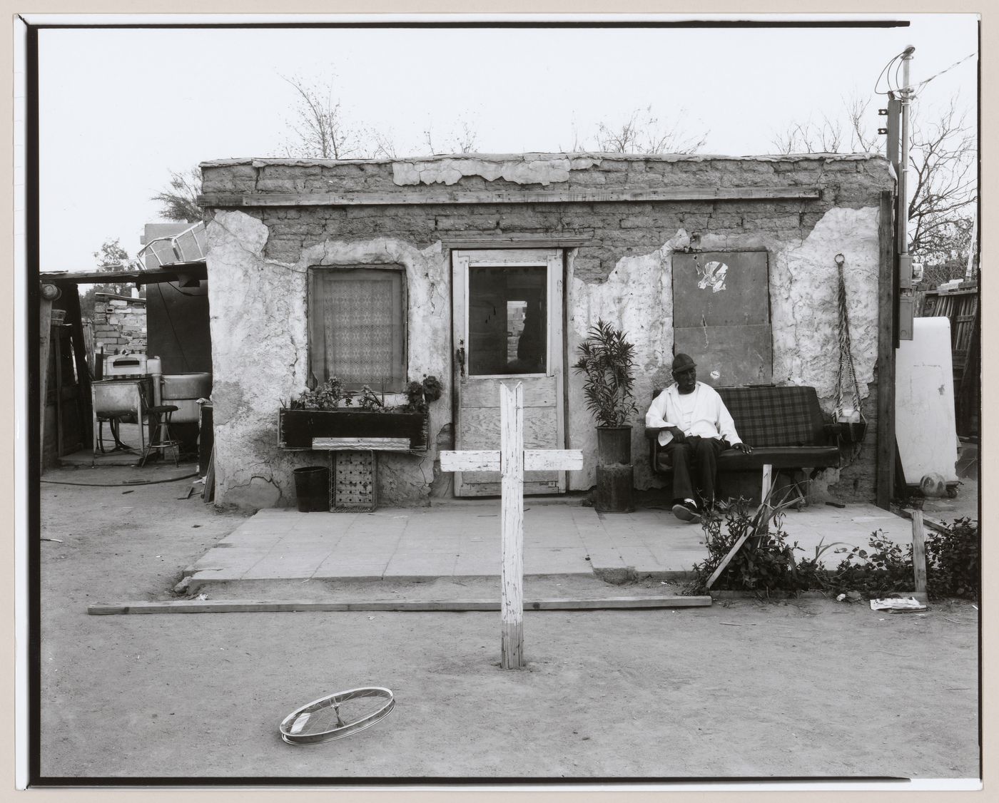 View of cross in yard in front of a house with a man sitting outside, Old Pascua, Tucson, Arizona, United States (from a series documenting the Yaqui community of Old Pascua)