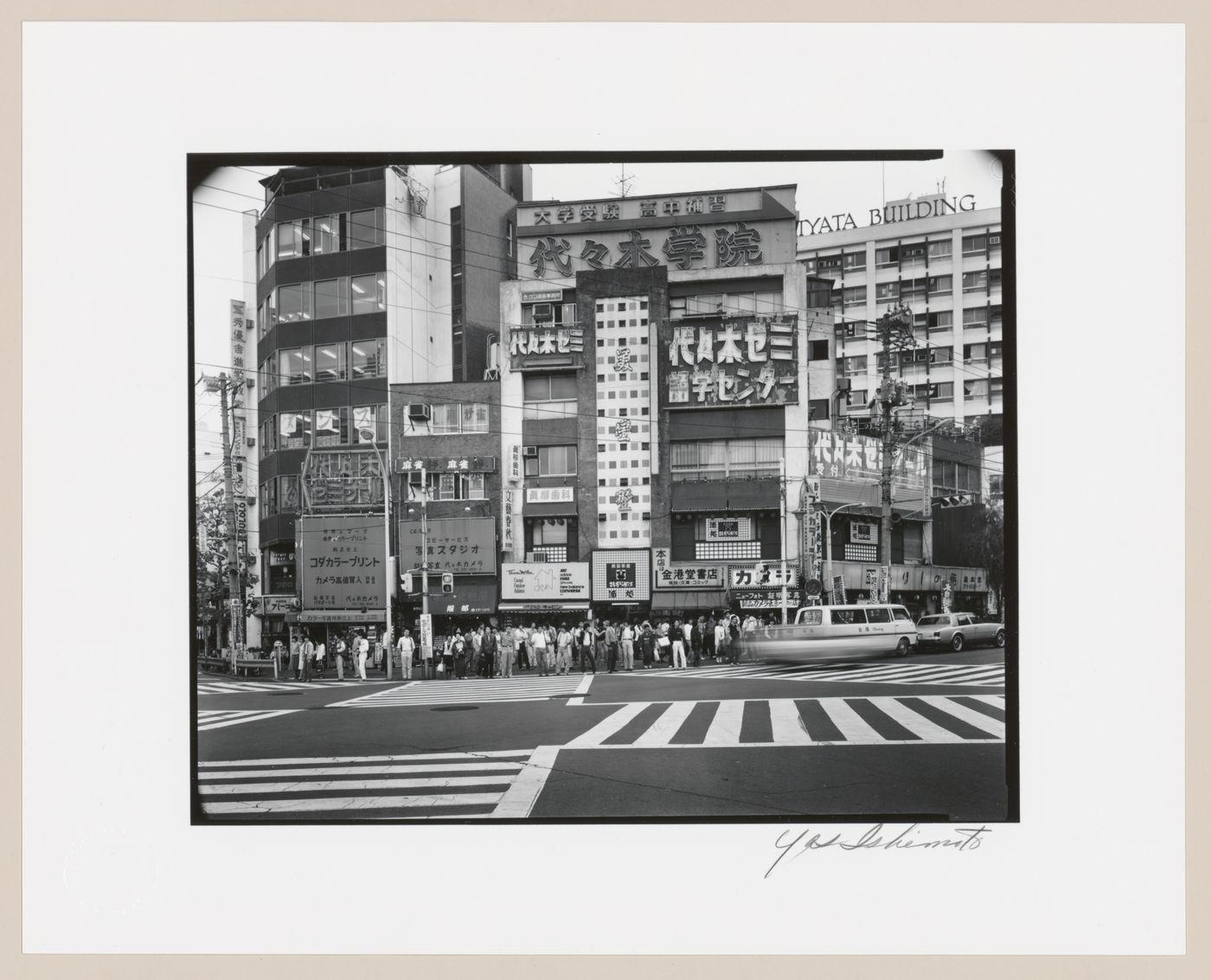 View of an intersection with pedestrian crossings and low-rise and mid-rise commercial buildings with outdoor advertising, in front of Yoyogi railway station, Shibuya, Tokyo, Japan.