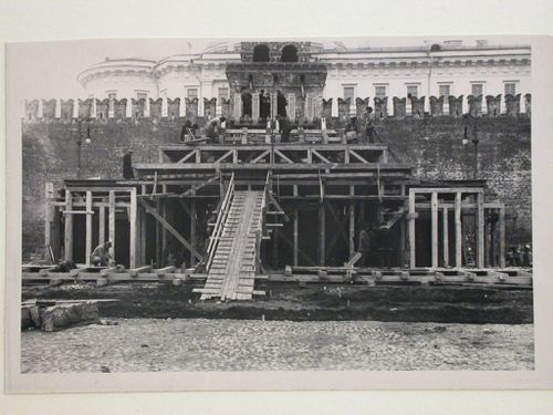 View of the principal façade of the second wooden Lenin Mausoleum under construction showing workers and officials on the roof, Red Square, Moscow