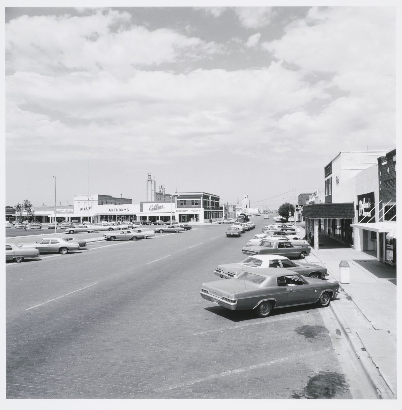 Town streets with cars, grain elevator in background, Brownfield, Texas