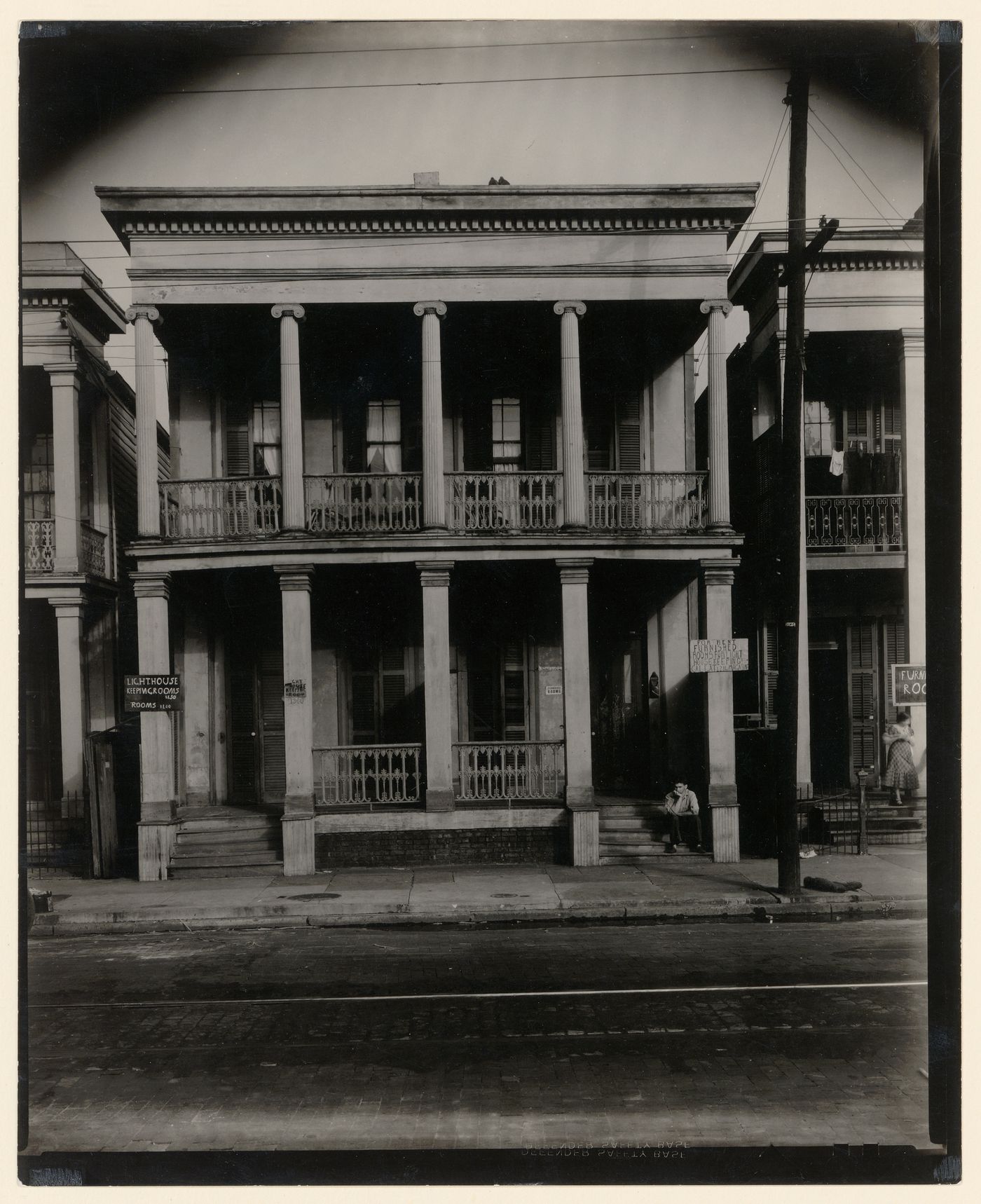 Boarding house: front view, man seated on steps, two-story house, women standing on step on the right, New Orleans