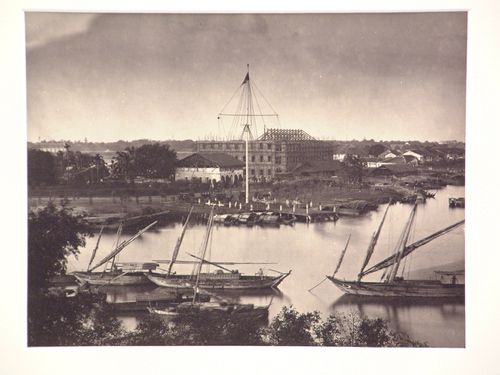 View of the flagtower and junks from across the Saigon River [?] with a building under construction in the background, Saigon (now Ho Chi Minh City), Cochin China (now in Vietnam)