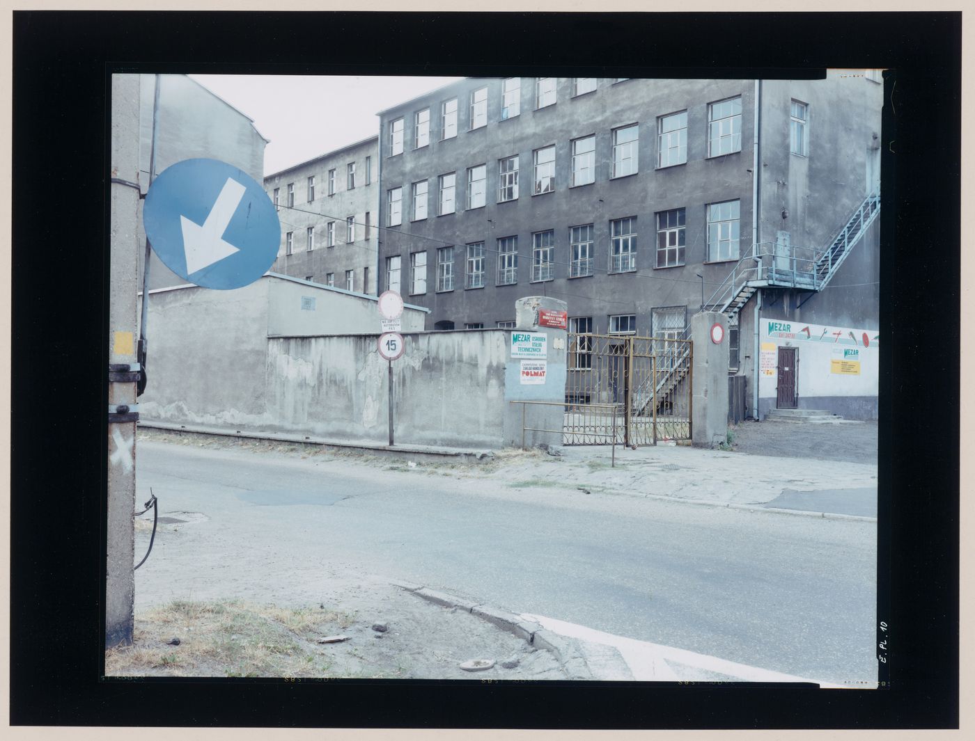 View of a building complex showing a gateway to a courtyard, the entrance to a tool store, a street and signs, Gorzów Wielkopolski, Poland (from the series "In between cities")