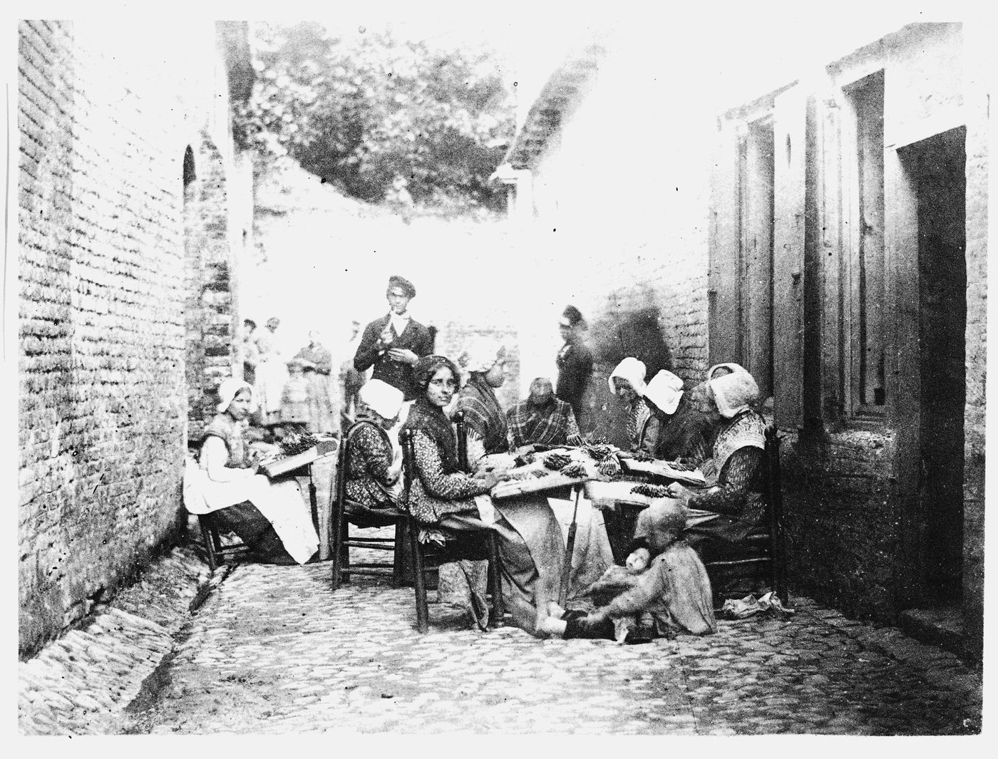 Women making lace in alley between two brick buildings, Flanders, Belgium