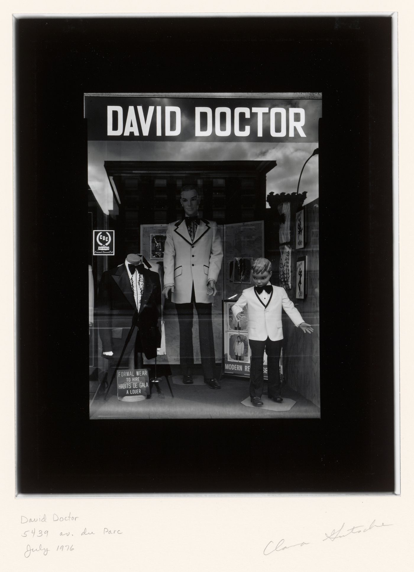 View of a display window of the David Doctor clothing store showing tuxedos and the reflection of buildings across the street, 5439 avenue du Parc, Montréal, Québec