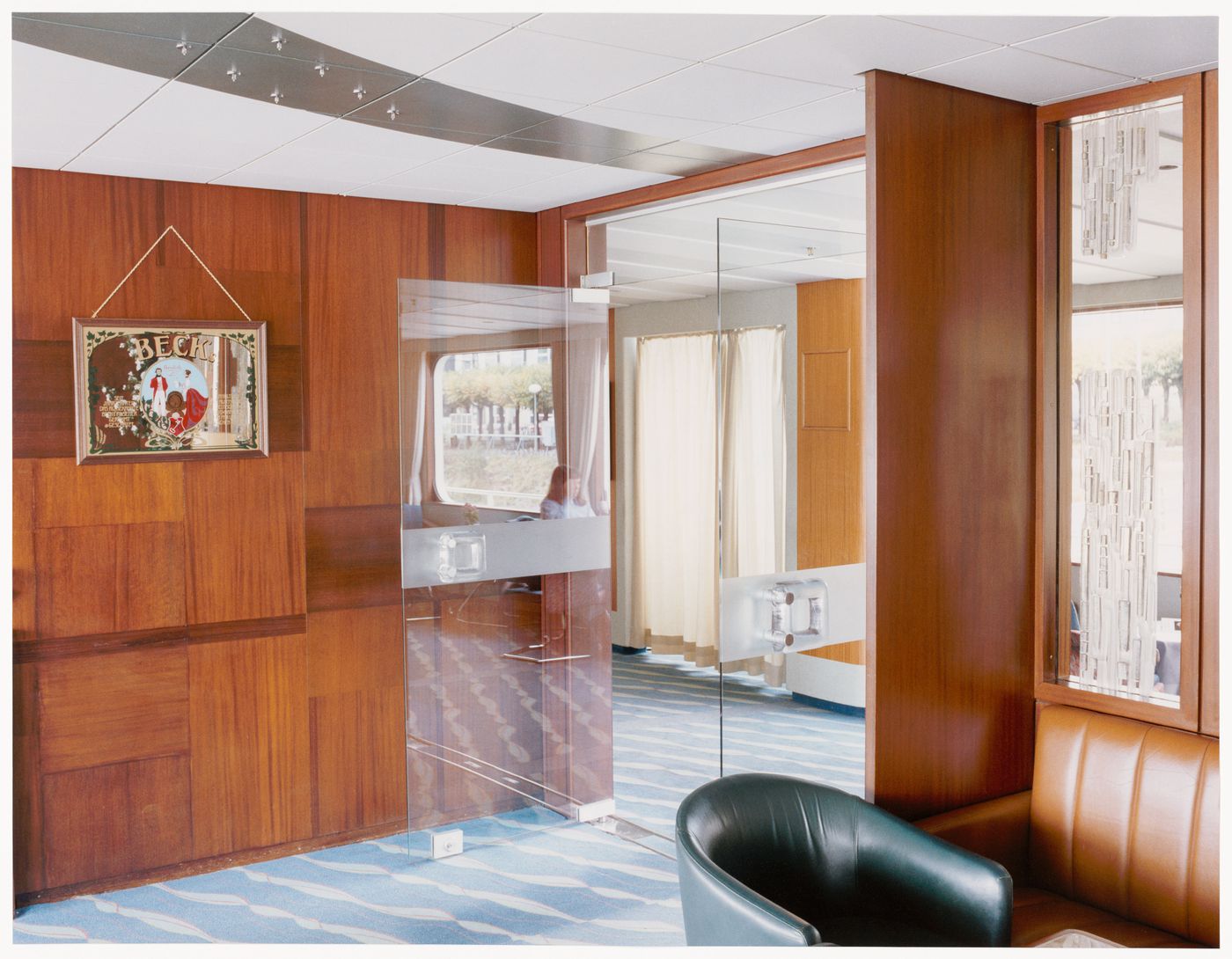 Interior view of a ship lounge with open glassed doors and panelled wood walls, New York