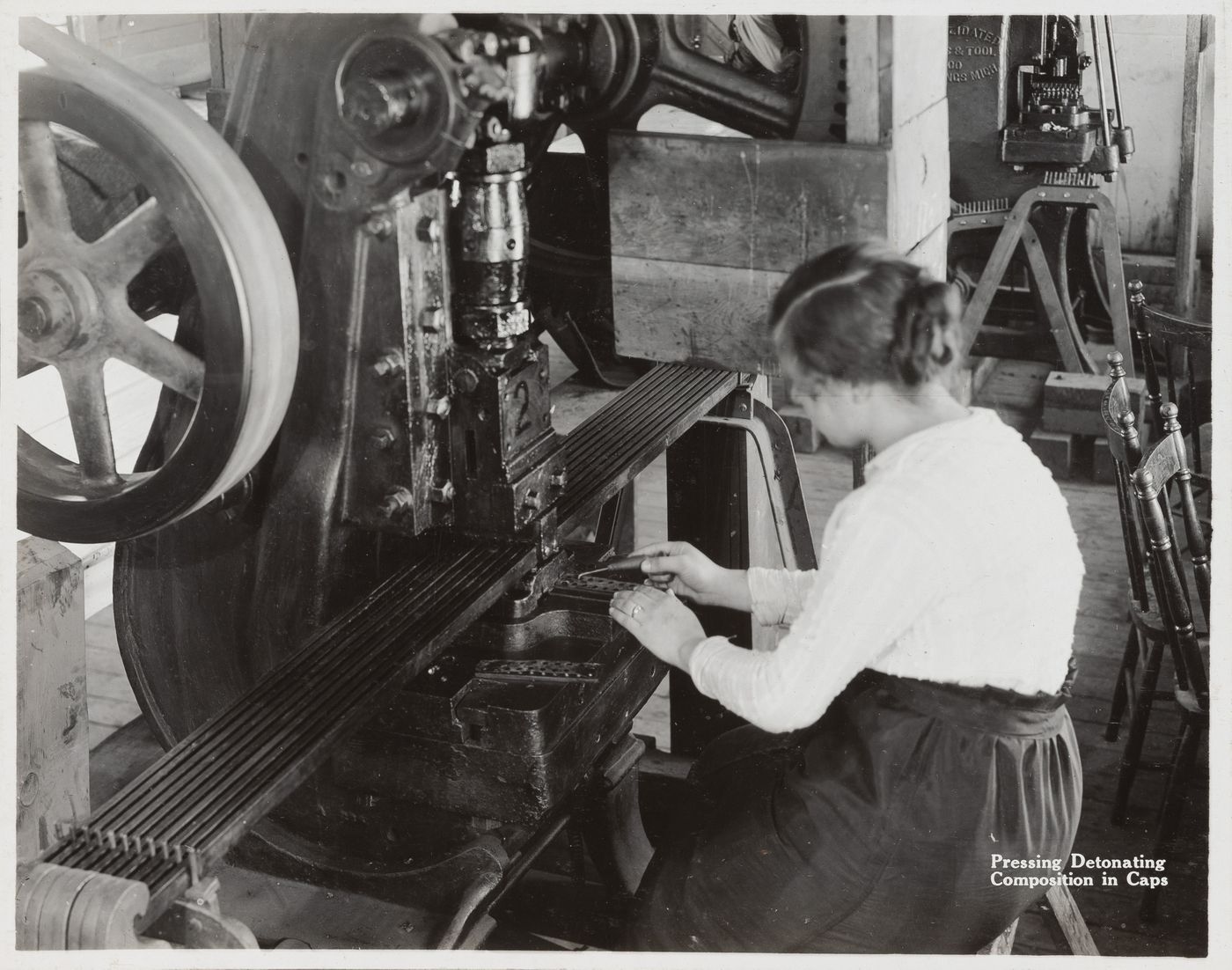 Interior view of worker pressing detonating composition in caps at the Energite Explosives Plant No. 3, the Shell Loading Plant, Renfrew, Ontario, Canada