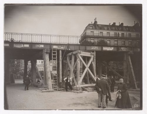 Construction of the Paris Metro, detail, exterior view with train on raised bridge with people standing under the bridge, Paris, France