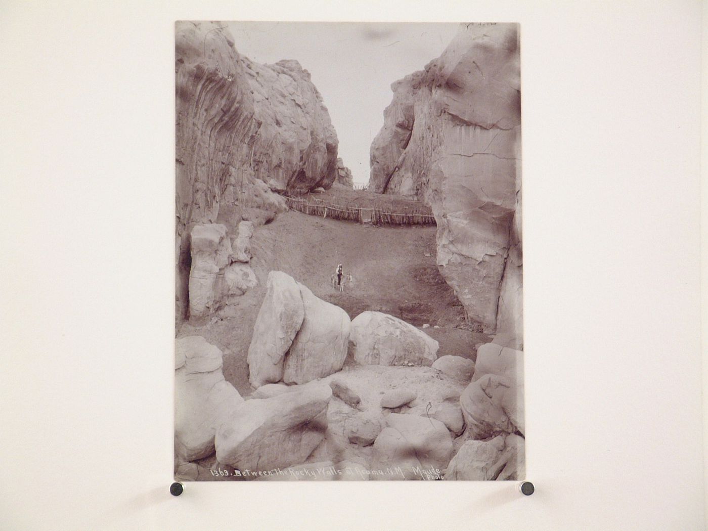 View through a canyon showing fences and a man riding a donkey down an embankment, Acoma, New Mexico, United States