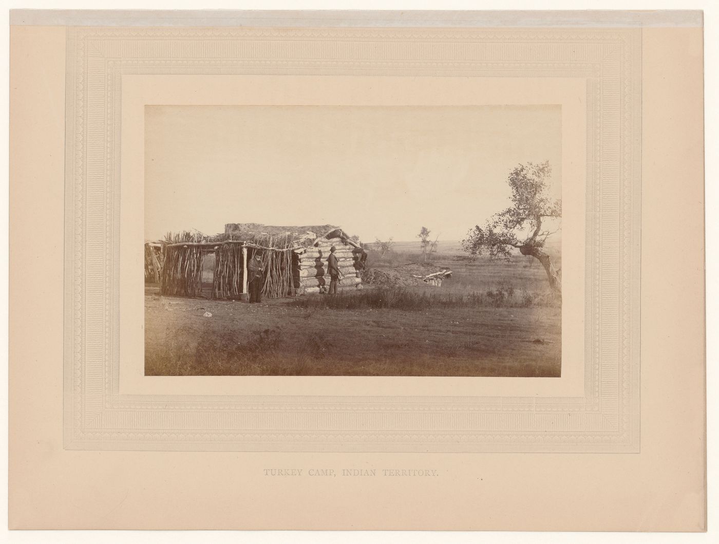 View of turkey hunting camp with two men in front of log cabin with sod roof, "Indian Territory" (now Oklahoma?), United States