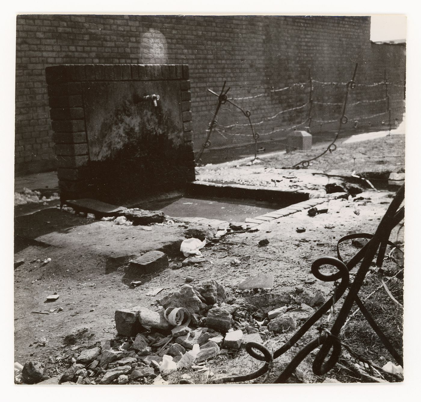 View of public water point with barbed wire fence in front of brick wall during construction of Chandigarh, India