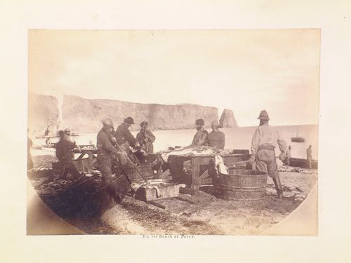 View of men preparing fish on the beach with Percé Rock in the background, Percé, Québec