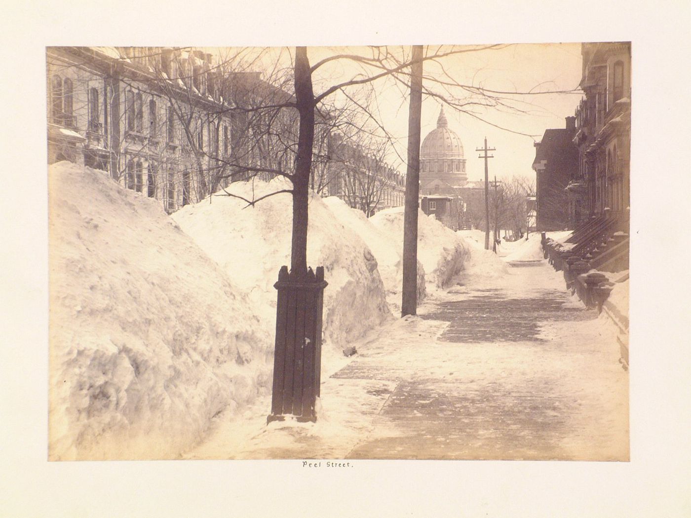View of rue Peel after a heavy snowfall with the dome of the Cathédrale Saint-Jacques-le-Majeur (now the Cathédrale Marie-Reine-du-Monde) in the background, Montréal, Québec