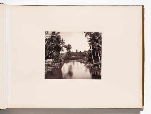 View of a river and its banks with a road and fence on the left, Ceylon (now Sri Lanka)