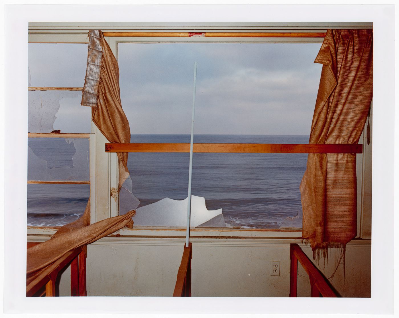 Abandoned beach house, interior, orange curtains framing broken window glass, California ?