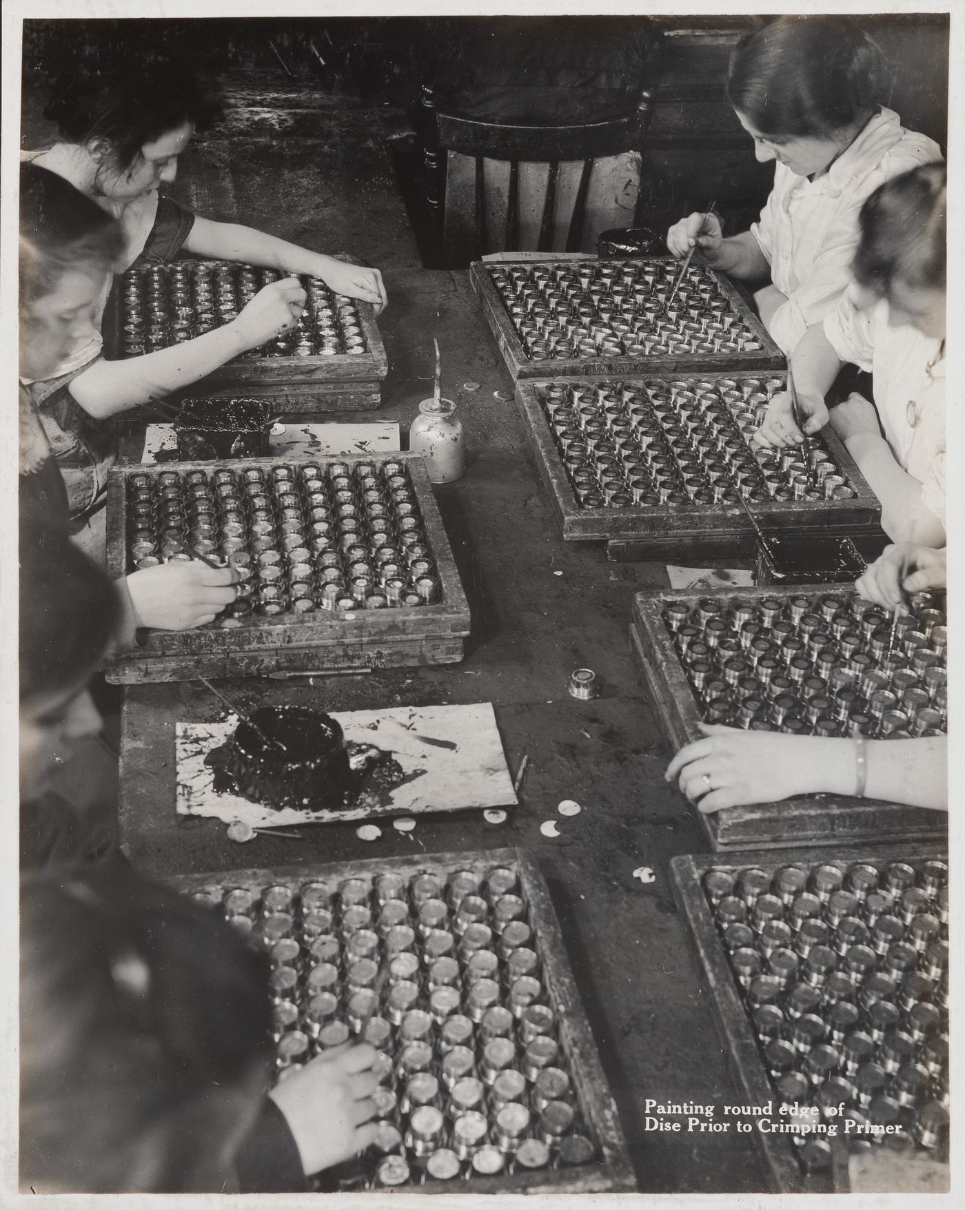 Interior view of workers painting round edge of disc prior to crimping primer at the Energite Explosives Plant No. 3, the Shell Loading Plant, Renfrew, Ontario, Canada