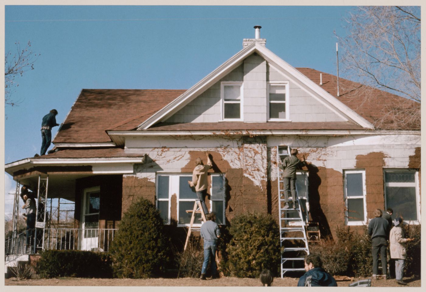 Photograph showing Pettena's team covering a house in clay for Clay House