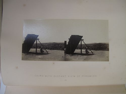 Stereographic view of person sitting on the roof of a house, with a view of the pyramids and city beyond, Cairo, Egypt