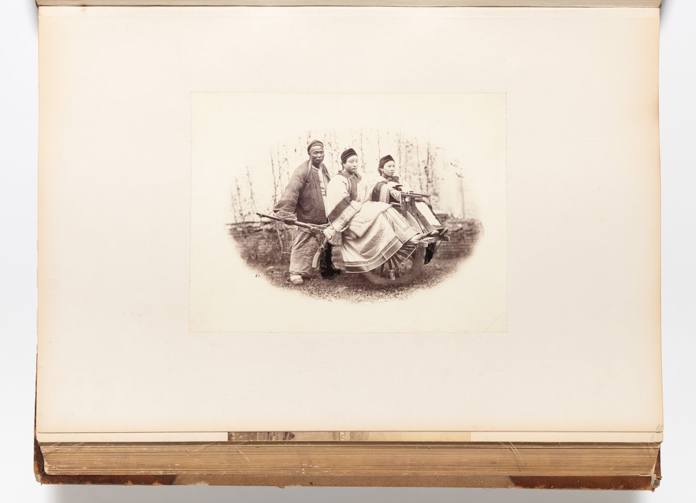 Vignette of two women riding in a wheelbarrow pushed by a man, Shanghai, China