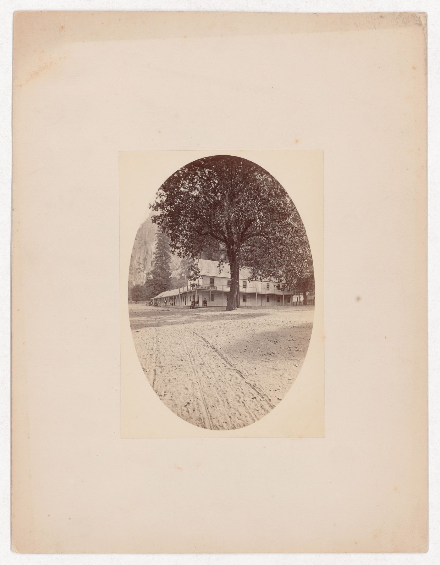 Road in foreground leading to Black's Hotel, two large trees, people out front, Yosemite Valley, California