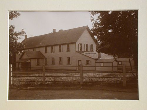 View of two-story, long, wooden building, bar fence in front of yard
