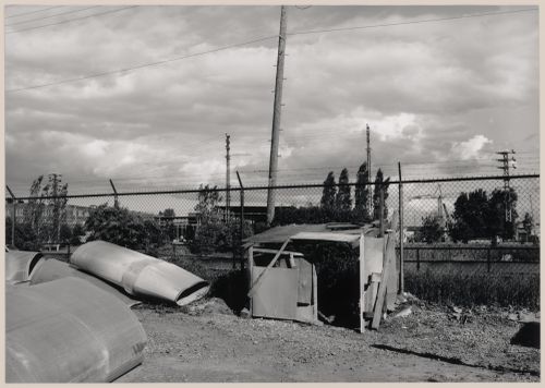 Field Work in Montreal: View of a wooden shack-like structure, air ducts, a chain link fence, utility poles and power lines, Montréal, Québec