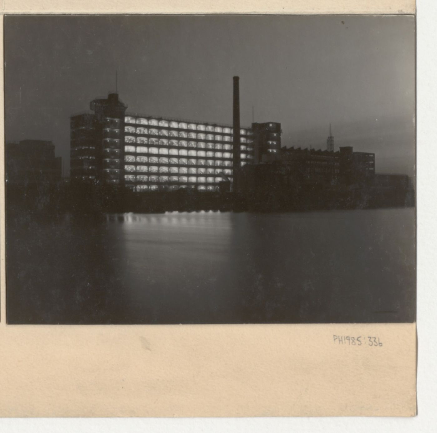 Exterior view of the Van Nelle Factory showing an illuminated office building from across the Rotte [?] River, Rotterdam, Netherlands