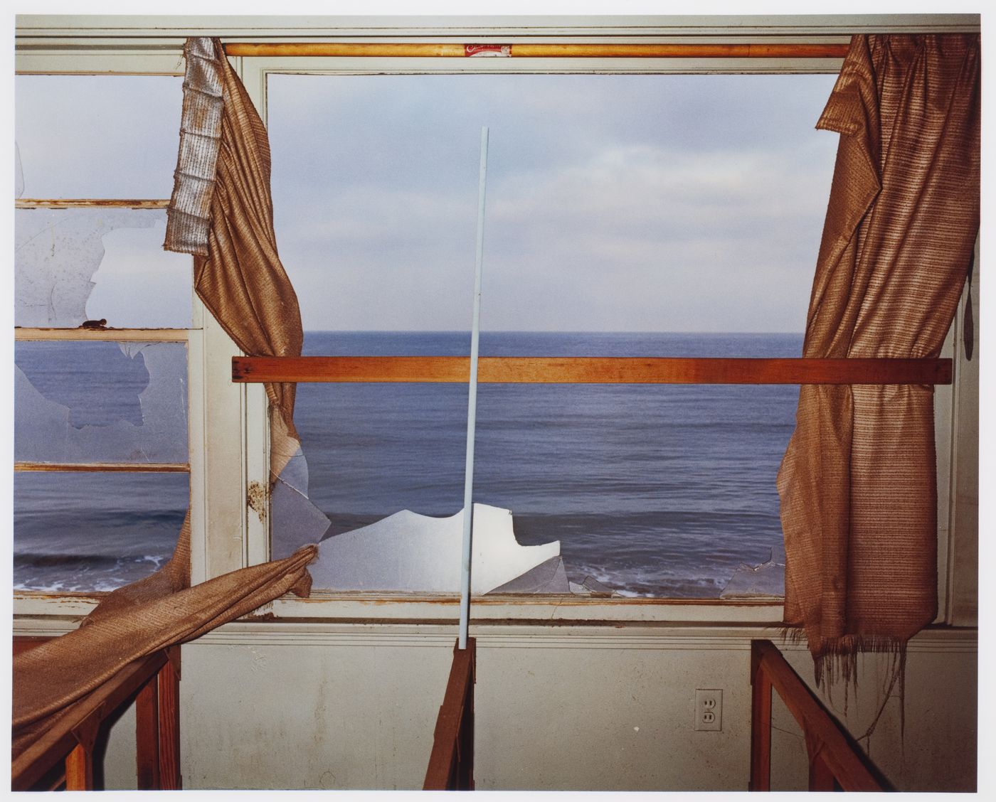 Abandoned beach house, interior, orange curtains framing broken window glass, California ?