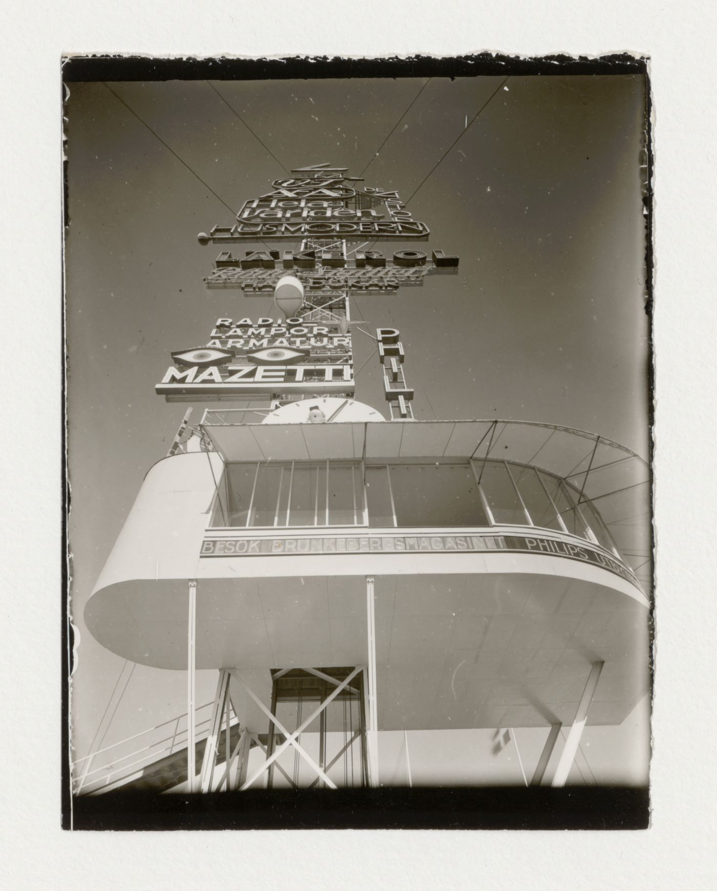 Worm's-eye view of the base of the advertising mast at the Stockholm Exhibition of 1930 showing a clock and neon lettering designed by Sigurd Lewerentz, Stockholm