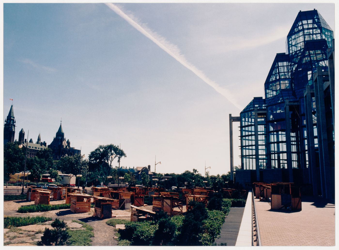 View of the installation "Favela in Ottawa", comprising wooden shack-like structures in the Taiga Garden of the National Gallery of Canada, showing the National Gallery and the Parliament Buildings, Ottawa, Ontario