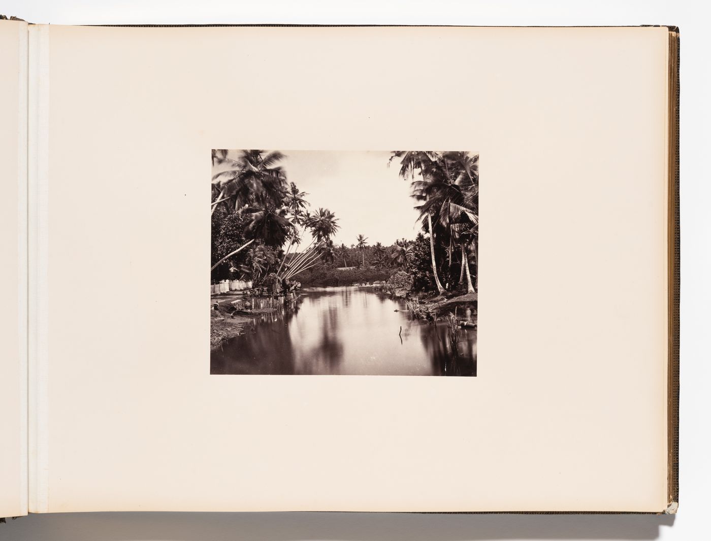 View of a river and its banks with a road and fence on the left, Ceylon (now Sri Lanka)