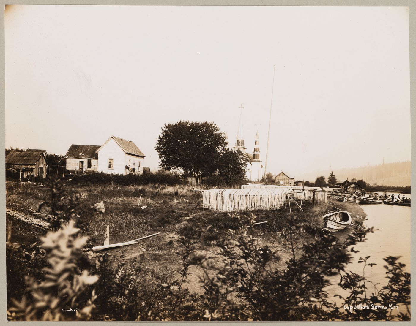 View showing Kwikwetlem First Nation community of slakəyánc (Coquitlam I.R. 1) with fish nets drying on racks, boats and Coquitlam River in the foreground and church in the background, Coquitlam, British Columbia, Canada