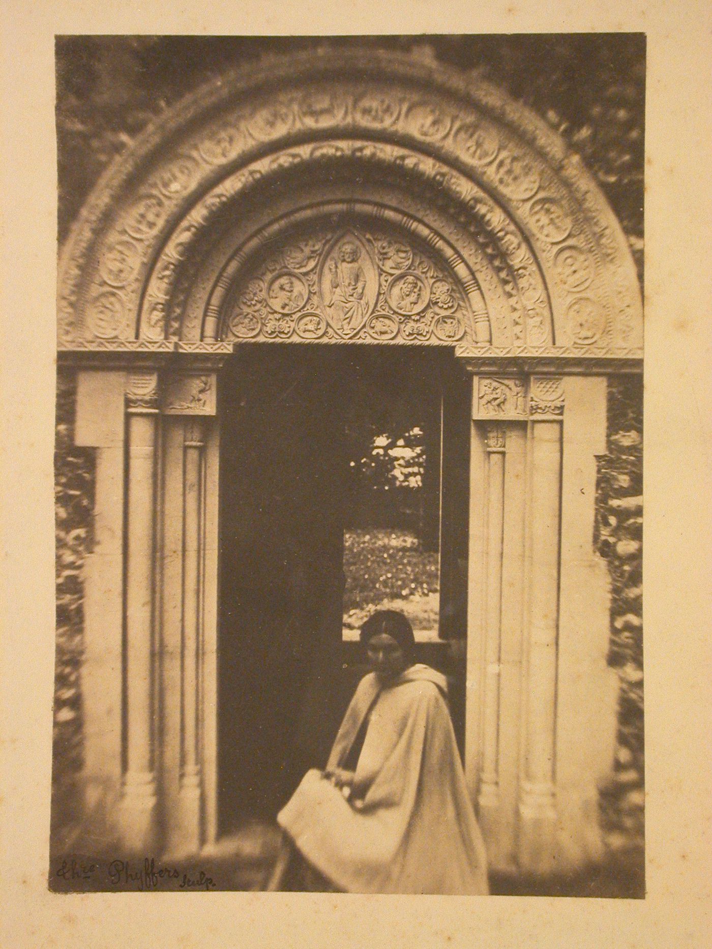 View of a woman standing in front of an ornamental doorway of a church [?], England [?]
